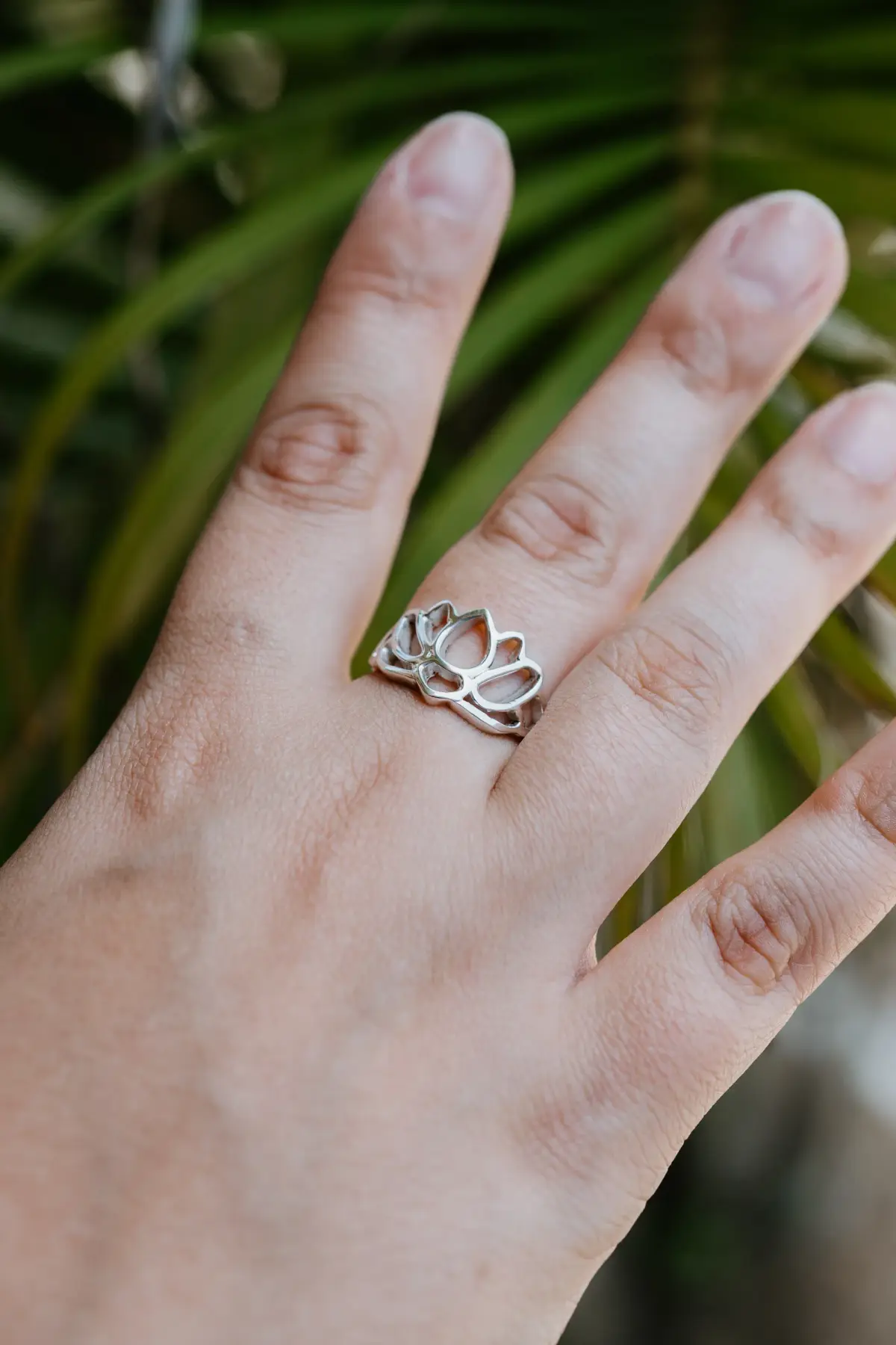 A lotus silver ring on a guest's hand among palm leaves